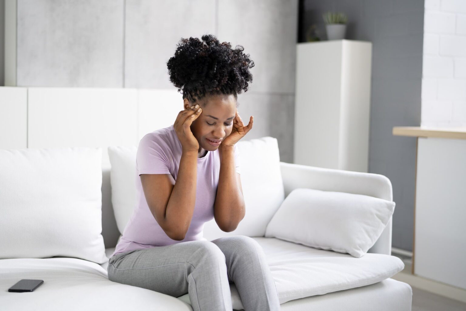 suffering from Benign paroxysmal positional vertigo Woman on the couch holding her temples lightly with her hands while experiencing a bppv spell